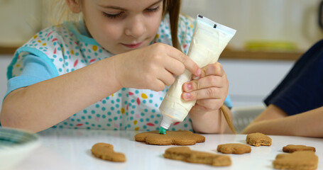 Little girl decorate cookies on table with icing. Cooking treats for celebration
