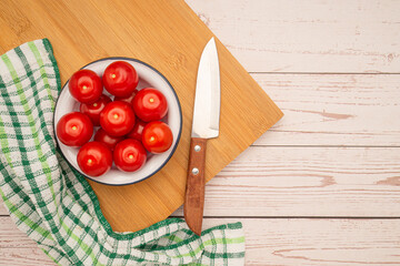 Fresh tomatoes on a plate and a knife with a cloth on a wooden cutting board over a table