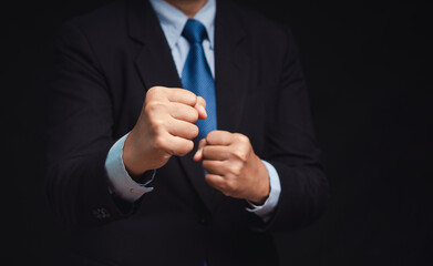 Businessman in a suit raised a fist while standing against a black background