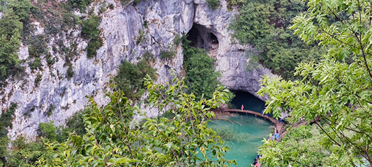 View of the lake and nature in the Plitvice Lakes National Park. Green water. Rocky mountains in the background. Tourists on a wooden bridge. Croatia. Europe