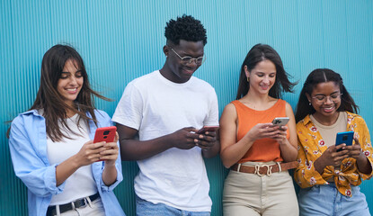Group of diverse young people using mobile phone outdoor. Friends having fun surfing on social media apps. Youth technology addicted. University students isolated in blue background.