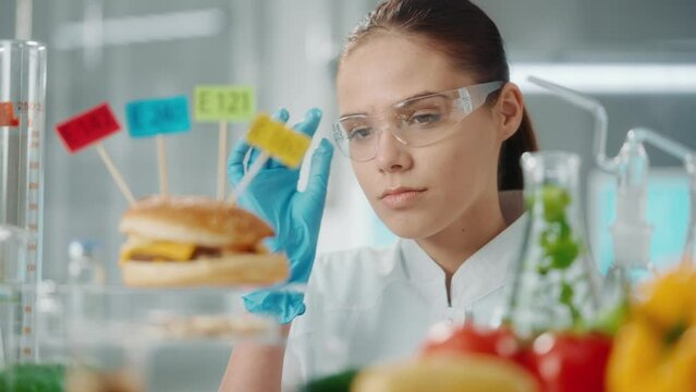 Young female researcher examines a sample of burger labeled E142, E240, E121 and E160. Biolog analyzes the quality of the sample. Close up.