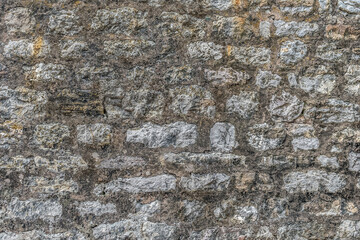 Gray real texture of old stone wall. Pattern of shapeless blocks with cement joints between them, covered with black fungus. Vintage architectural background with copy space
