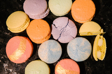 Fototapeta na wymiar Macaroons lie on a black marble table. Several macarons desserts are crushed and broken. Macarons closeup