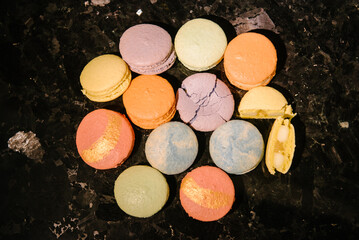 Macaroons lie on a black marble table. Several macarons desserts are crushed and broken.