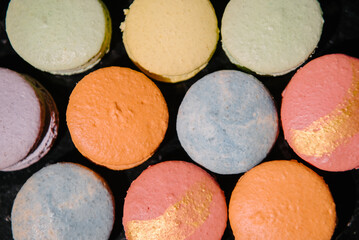 Obraz na płótnie Canvas Macaroons lie on a black marble table. Several macarons desserts are crushed and broken. Macarons closeup