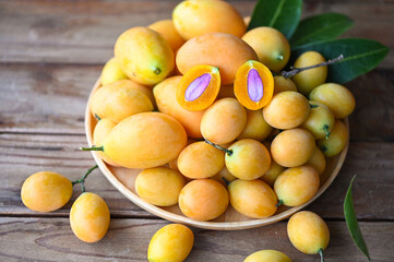 Naklejka na ściany i meble Marian plum fruit and leaves in plate on wooden background, tropical fruit Name in Thailand Sweet Yellow Marian Plum Maprang Plango or Mayong chid
