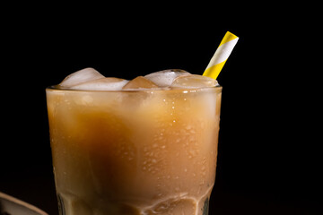 Close-up of a Cappuccino with Ice cubes in a tall Glass against a black background. Iced Coffee with milk in a glass
