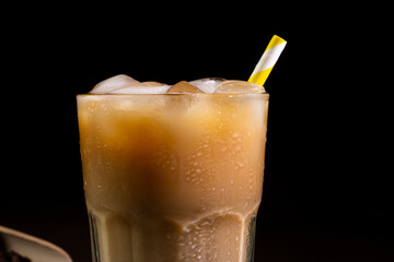 Close-up of a Cappuccino with Ice cubes in a tall Glass against a black background. Iced Coffee with milk in a glass