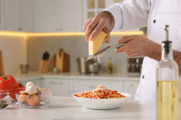 Professional chef grating cheese into delicious dish at white marble table indoors, closeup. Space...