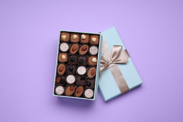 Open box of delicious chocolate candies on violet background, top view