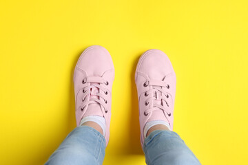 Woman in stylish sneakers standing on yellow background, top view