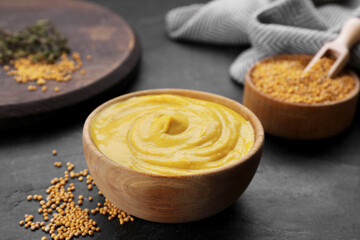 Bowl with delicious mustard and seeds on black textured table, closeup