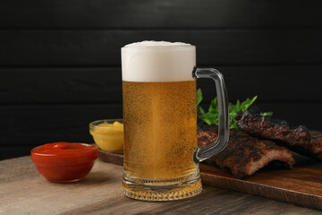 Mug with beer, delicious grilled ribs and sauces on wooden table
