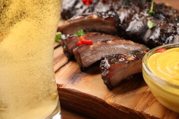 Glass of beer, tasty grilled ribs and sauce on wooden table, closeup