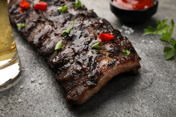 Tasty grilled ribs and sauce on grey table, closeup