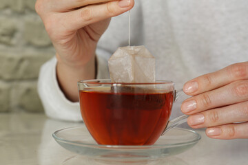 Woman taking tea bag out of cup at table indoors, closeup