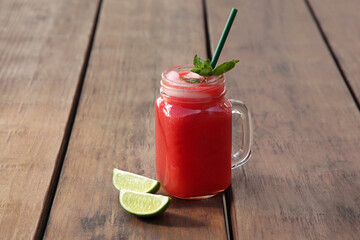 Delicious watermelon drink in mason jar and fresh lime on wooden table