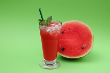 Glass of delicious drink with mint, ice cubes and cut fresh watermelon on light green background