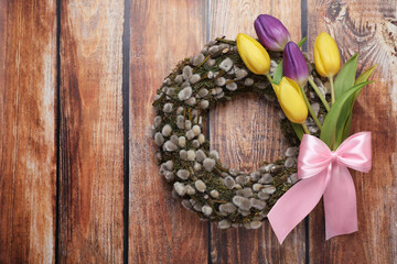 Wreath made of beautiful willow, colorful tulip flowers and pink bow on wooden background, top view. Space for text © New Africa