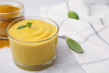 Tasty curry sauce, powder and basil leaves on white table, closeup. Space for text
