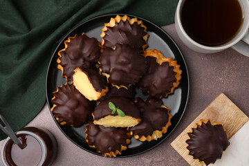 Delicious profiteroles with chocolate spread, cream and aromatic tea on textured table, flat lay
