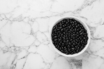 Fototapeta na wymiar Bowl of raw black beans on white marble table, top view. Space for text