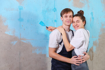 Obraz na płótnie Canvas House decoration DIY renovation concept. Happy couple during repair in empty room of new home painting wall together. Husband and wife hugging in new house. Happy family doing home renovation