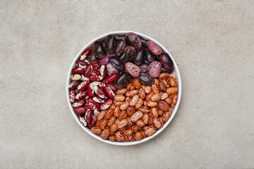 Bowl with different types of beans on light grey table, top view