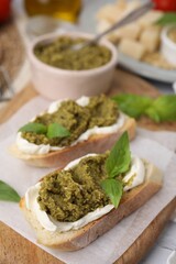 Tasty bruschettas with cream cheese, pesto sauce and fresh basil on wooden board, closeup
