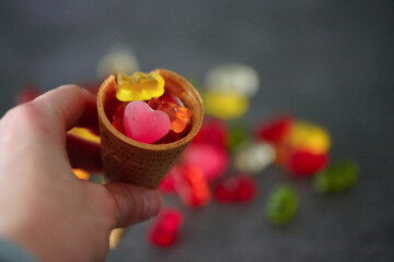 Closeup shot of a hand holding a waffle cone with colorful jellies on top