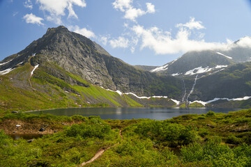 Scenic view of a calm lake surrounded by mountains covered with green grass and snow patches