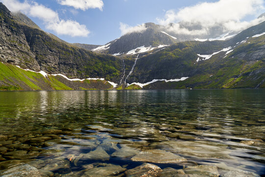 Calm lake with transparent water surrounded by rocky mountains covered with snow patches