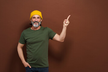 Smiling European man in a yellow hat points his hand to the side with copy space on a brown...