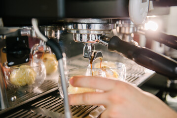Coffee machine. Coffee is poured from the holder into glass cups. Ice cream scoops in glasses. Barista holding a glass with his hand