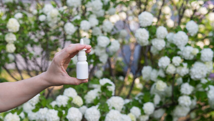 Woman's hand with a nasal spray on a background of a flowering tree. 