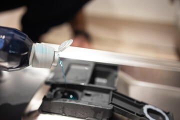Close up of a man pouring a rinse into the compartment of a dishwasher. Household chores, house cleaning, cleaning, repair and maintenance of equipment. Selective focus