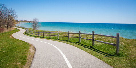 Obraz premium Asphalt road with a wooden fence along the blue sea under the clear sky