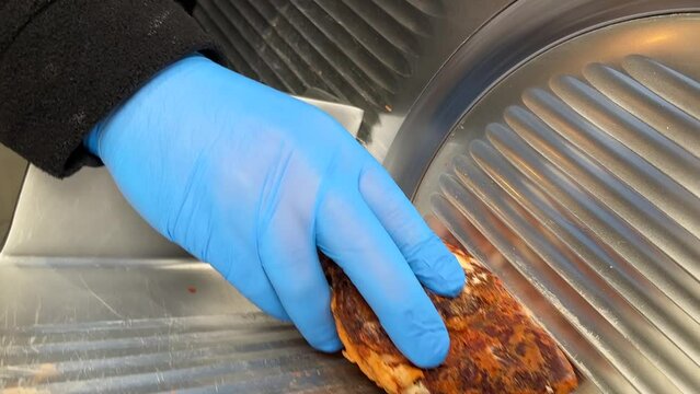 Turkish pastrami cut into thin slices. Chopping Turkish bacon on an electric food slicer. Slicing bacon with machine.