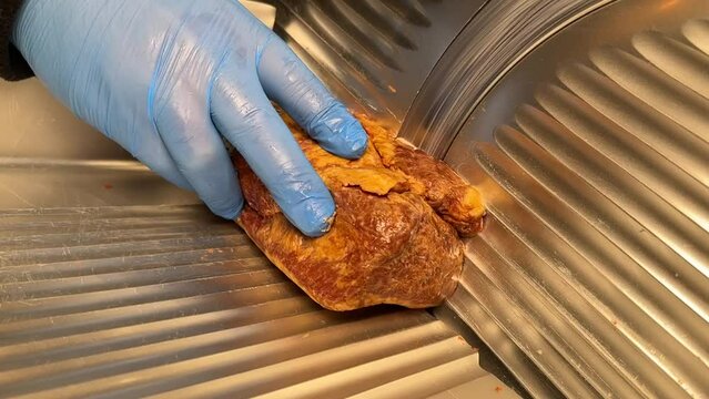 Turkish pastrami cut into thin slices. Chopping Turkish bacon on an electric food slicer. Slicing bacon with machine.