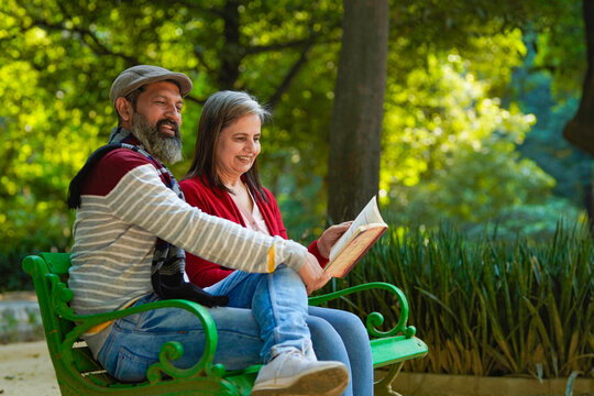 Indian senior man and woman reading book at park.