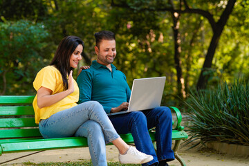 Young indian couple using laptop at park.