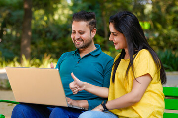 Young indian couple using laptop at park.