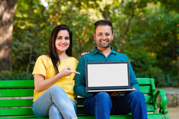 Indian man and woman showing laptop screen at park