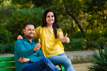 Fototapeta premium Happy young indian man and woman showing thumps up at park.