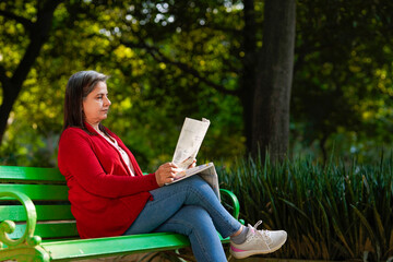 Senior Indian woman reading newspaper at park.