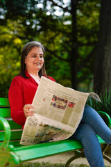 Senior Indian woman reading newspaper at park.