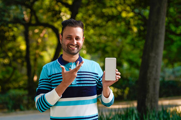 Indian man showing smartphone screen at park.