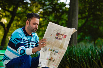 Young indian man reading news paper at park.