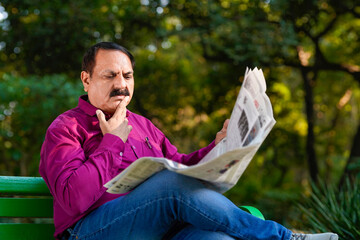 Indian old man reading news paper at park.